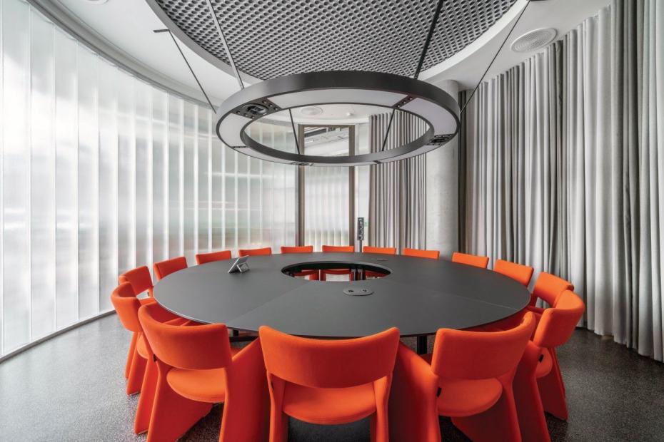 Im Erdgeschoss geben runde Besprechungsinseln runde Deckenleuchten und Tische sowie orangefarbene Stühle den Ton an.