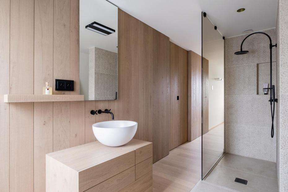 Das große Bad verfügt über ein offenes Raumgefüge, verbunden mit gebleichtem Eichenholz, Naturstein und weißen Wandflächen. 