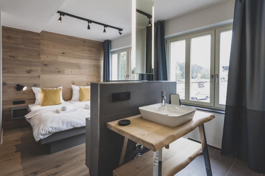 In einigen Zimmern ist der Waschplatz der Serie „Cape Cod“ offen in das Schlafzimmer integriert, hier in Verbindung mit einem von der Decke hängendem und seitlich beleuchteten Spiegel.